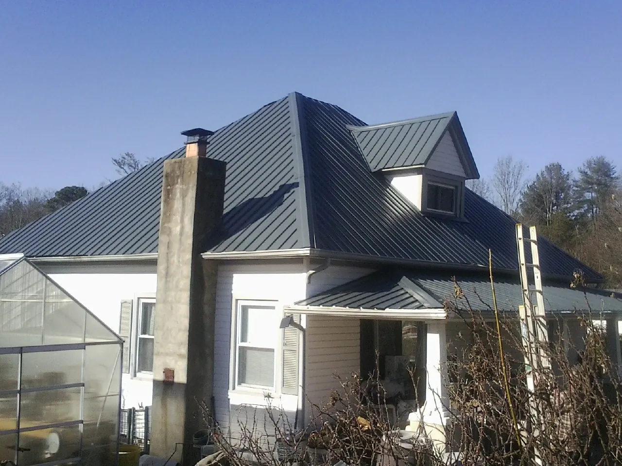 Dark blue standing seam metal roof on a white farmhouse with dormer — Slate & Tile Roof Repair by Roofing Brothers in Ivydale