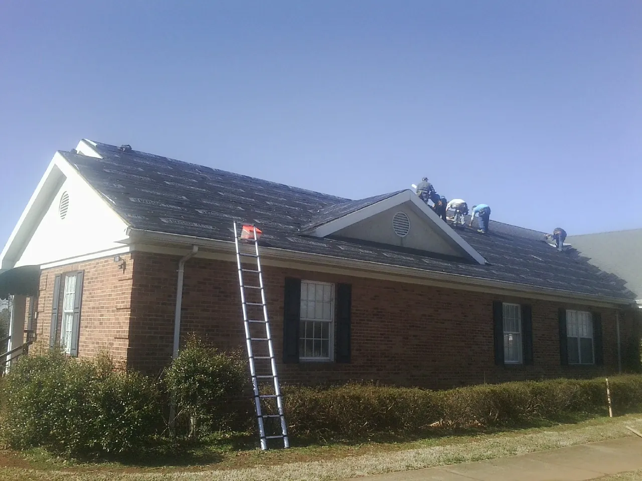 Crew tearing shingles off a brick ranch roof with a ladder set — Metal Roof Repair work by our crew in Ivydale