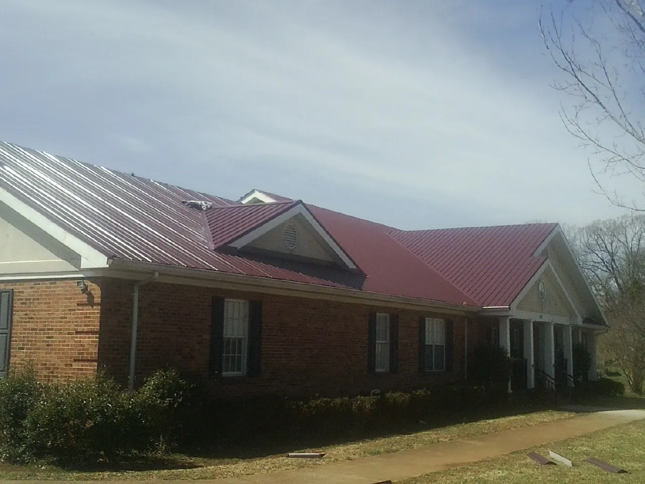 Red metal roof with gabled entries on a long brick building, from a Hail Damage Roof Repair job in Ivydale