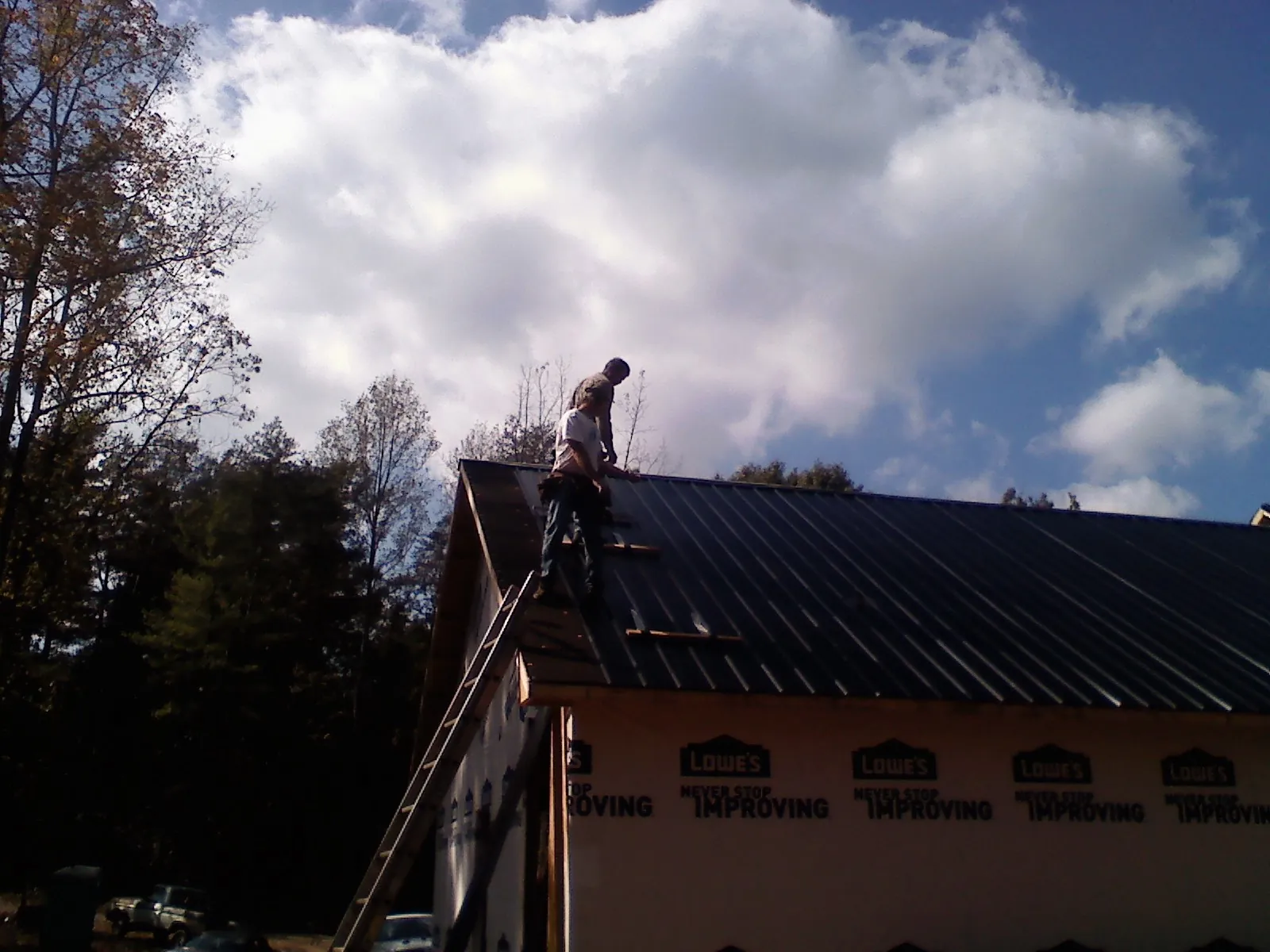 Roofer fastening dark metal panels high against a cloudy sky, from a Roof Inspection job in Ivydale