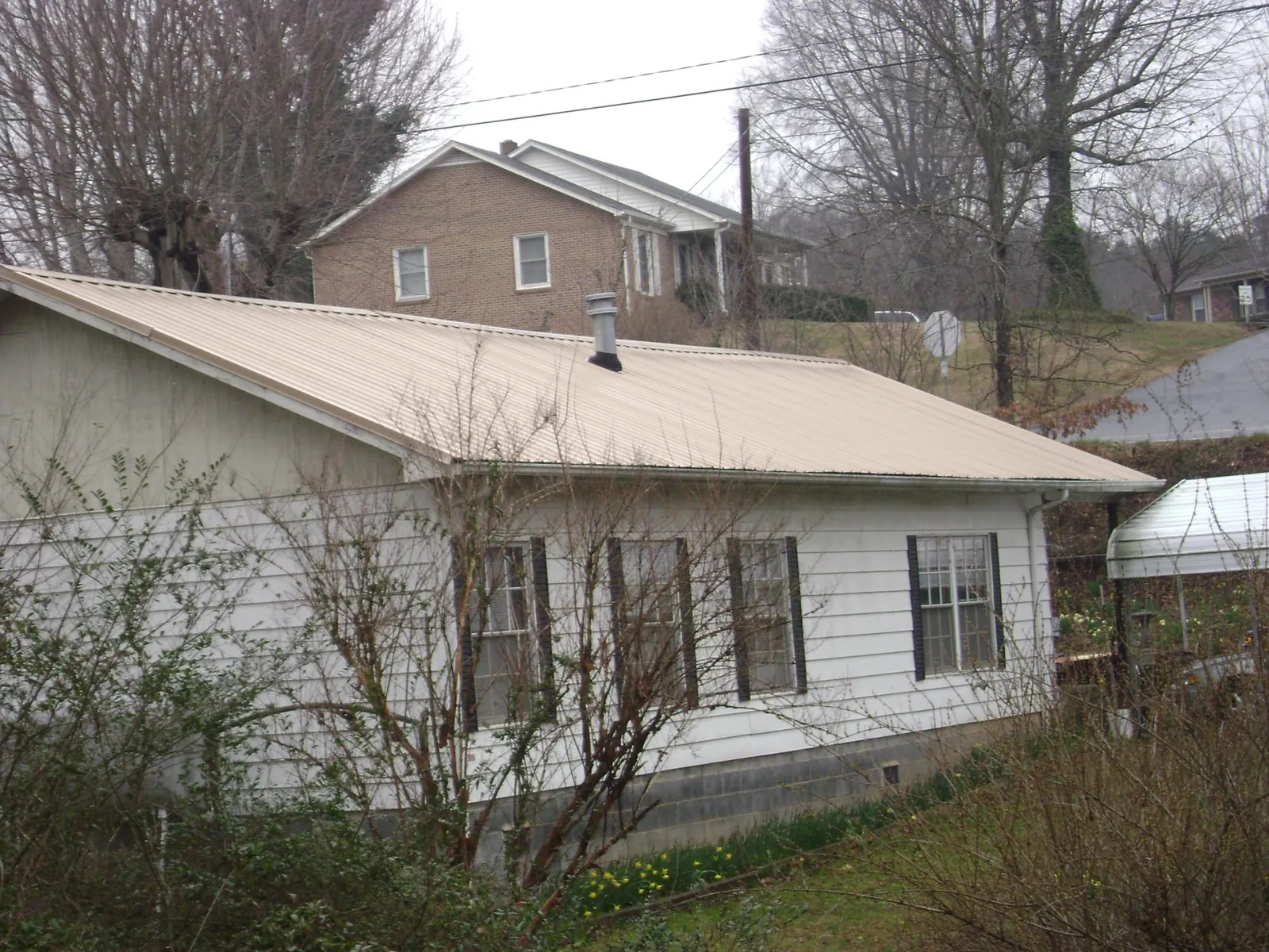 Tan metal roof on a white sided house set into a hillside — Commercial Roofing by Roofing Brothers in Ivydale